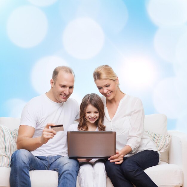 Familien-, Feiertags-, Einkaufs-, Technologie- und Leutekonzept - glückliche Familie mit Laptop-Computer und Kreditkarte über Blaulichthintergrund