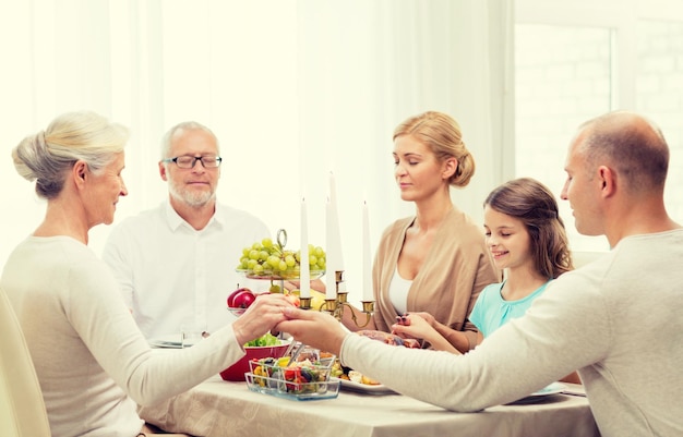 Familien-, Feiertags-, Generations- und Personenkonzept - lächelnde Familie, die zu Hause zu Abend isst und betet