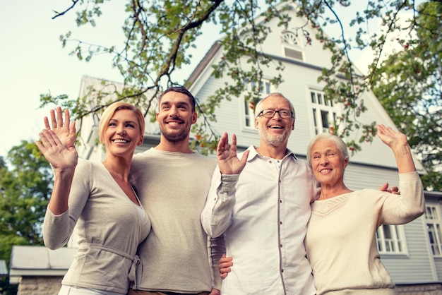 Familien-, Generations-, Heim-, Gesten- und Personenkonzept - glückliche Familie, die vor dem Haus steht und draußen mit den Händen winkt