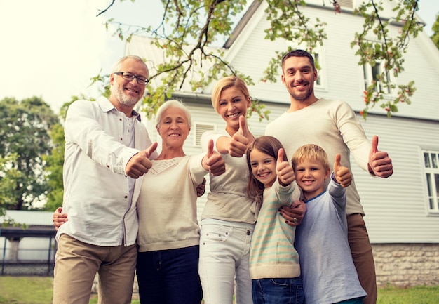 Familien-, Glücks-, Generations-, Heim- und Menschenkonzept - glückliche Familie, die vor dem Haus steht und Daumen nach oben zeigt