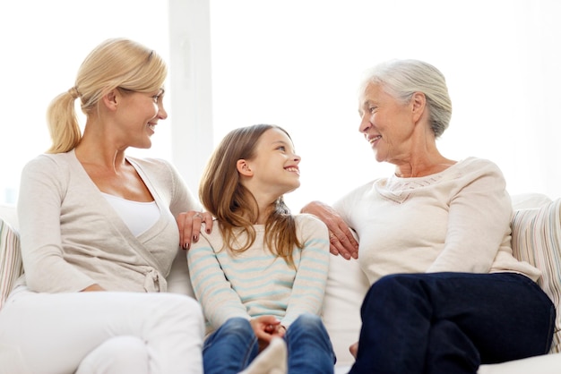 familien-, glücks-, generations- und personenkonzept - lächelnde mutter, tochter und großmutter, die zu hause auf der couch sitzen