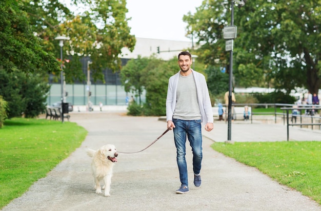 Familien-, Haustier-, Tier- und Personenkonzept - glücklicher Mann mit Labrador-Retriever-Hund, der im Stadtpark spazieren geht