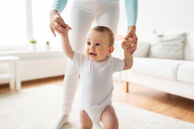 Familien-, Kinder-, Kindheits- und Elternschaftskonzept - glückliches kleines Baby, das zu Hause mit der Hilfe der Mutter laufen lernt