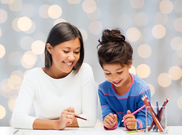 Familien-, Kinder-, Kreativitäts- und glückliche Menschenkonzept - glückliche Mutter- und Tochterzeichnung mit Bleistiften über Feiertagen beleuchtet Hintergrund