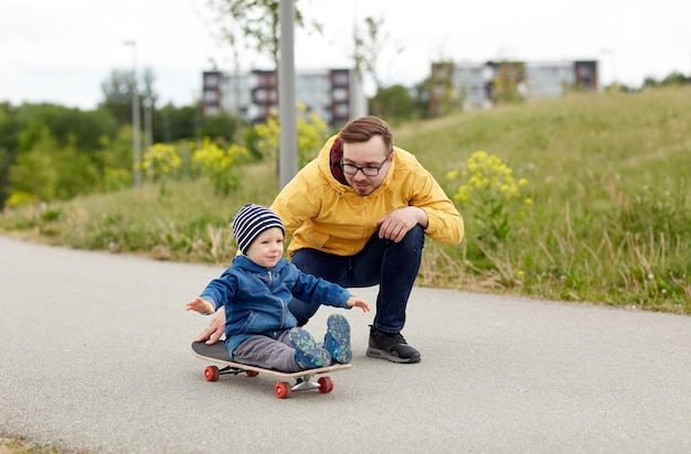 Familien-, Kindheits-, Vaterschafts-, Freizeit- und Menschenkonzept - glücklicher Vater und kleiner Sohn fahren auf Skateboard