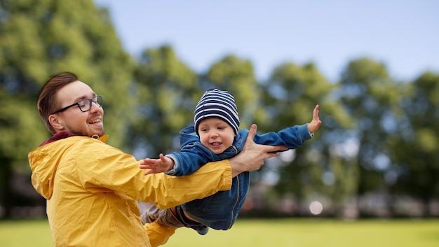 Familien-, Kindheits-, Vaterschafts-, Freizeit- und Menschenkonzept - glücklicher Vater und kleiner Sohn spielen und Spaß haben im Freien vor sommerlichem Parkhintergrund