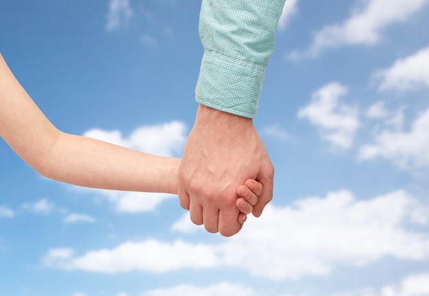Familien-, Kindheits-, Vaterschafts- und Menschenkonzept - Vater und Kind halten Hände über blauem Himmel und Wolkenhintergrund
