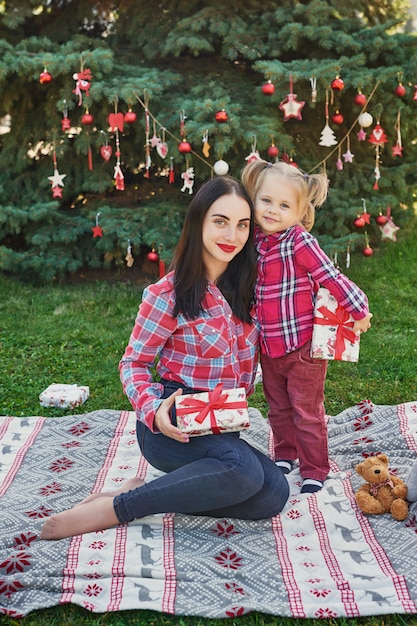 Familien-Neujahrsfotosession der Mutter und der Tochter im Juli nahe dem Weihnachtsbaum mit Geschenken im Park