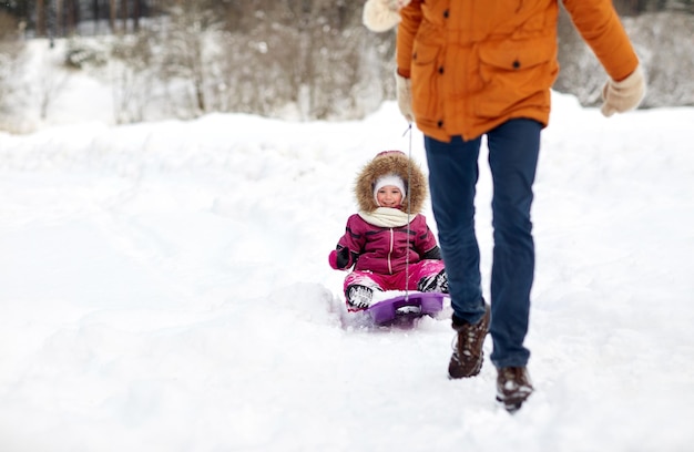 Foto familien-, rodeln-, jahreszeiten- und personenkonzept - vater zieht schlitten mit glücklichem kind im freien im winter
