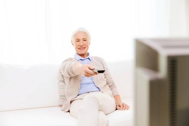 Familien-, Technologie-, Fernseh-, Alters- und Personenkonzept - glückliche Seniorin, die zu Hause fernsieht