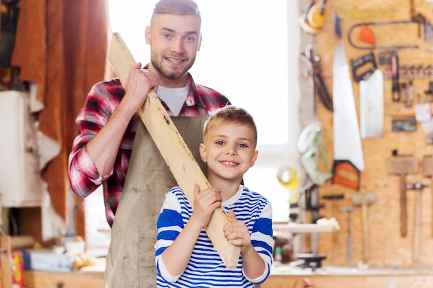 Familien-, Tischler-, Holzarbeiten- und Personenkonzept - glücklicher Vater und kleiner Sohn mit Holzbrett in der Werkstatt
