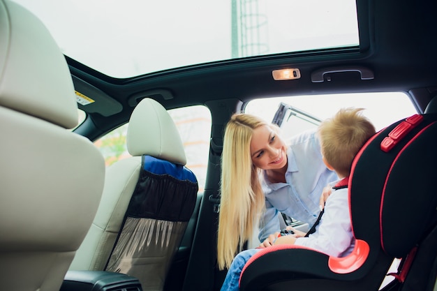 Familien-, Transport-, Roadtrip- und Personenkonzept - glückliche Frau, die Kind mit Sicherheitsgurt im Auto befestigt