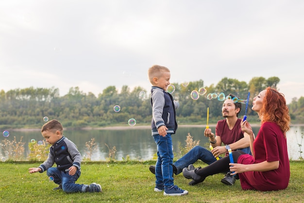 Familien- und Naturkonzept. Mutter, Vater und ihre Kinder spielen mit bunten Seifenblasen