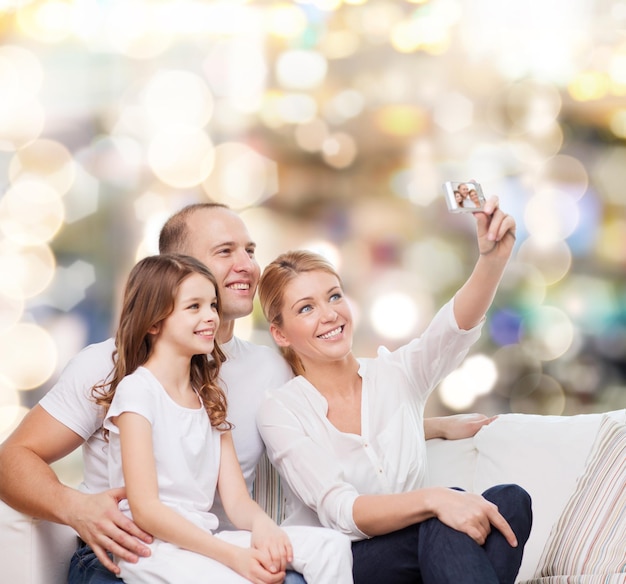 Familien-, Urlaubs-, Technologie- und Personenkonzept - lächelnde Mutter, Vater und kleines Mädchen machen Selfie mit Kamera über hellem Hintergrund