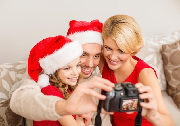 Familien-, Weihnachts-, Weihnachts-, Glücks- und Personenkonzept - lächelnde Familie in Weihnachtsmannmützen, die ein Foto mit einer Fotokamera machen