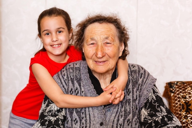 Familienbindungskonzept. Schönes kleines Mädchen, das glücklich ihre Oma im hellen Wohnzimmer umarmt