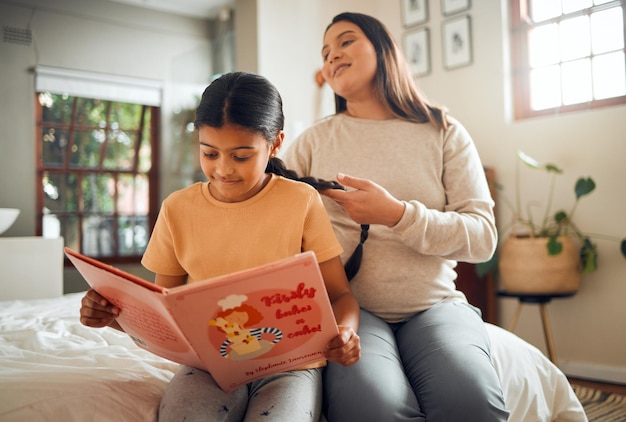 Familienbuch oder Bildung und ein Mädchen, das in einem Schlafzimmer liest, während ihre Mutter mit ihren Haaren in ihrem Haus spielt Bücher lernen und lieben mit einer Mutter und Tochter, die sich verbinden, während sie zusammen auf einem Bett sitzen