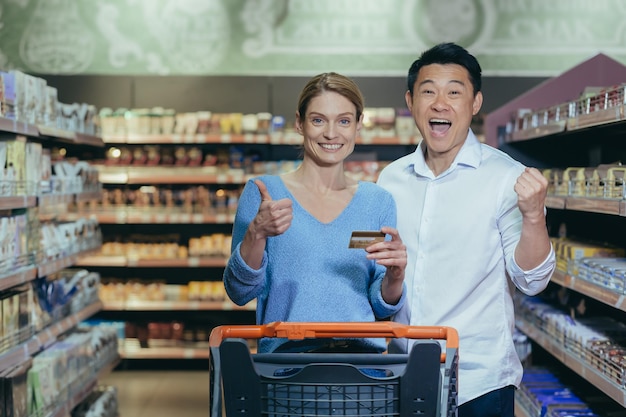 Familieneinkauf Junges schönes interraciales Paar, das in einem Supermarkt glückliche asiatische Frau einkauft und