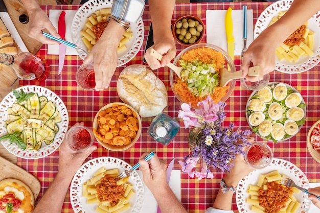 Familienessen mit bunt karierter Tischdecke Viele Hände, die Essen nehmen