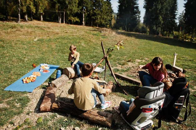 Familienfeuer im Berg. Braten von Würstchen. Mutter mit vier Kindern, die campen. Herbstwanderung und Lagerwetter. Erwärmen und Kochen in der Nähe der Flamme zusammen.