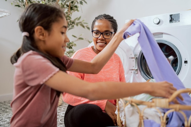 Familienhilfe bei der Hausarbeit Wäsche in die Waschmaschine legen bunte schmutzige Sachen, die das Mädchen aus dem Weidenkorb holt, werden der Mutter gegeben