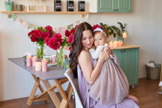 Familienmutter und -tochter mit Pfingstrosenblumen in der Küche zu Hause. Glückliche Mutter und kleine Tochter. Glückliche Familie.