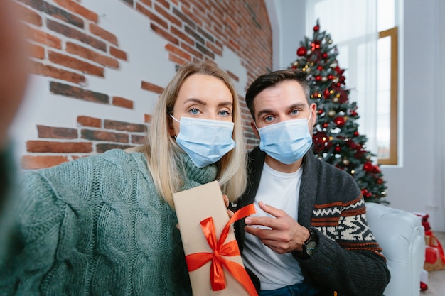 Familienpaar in Liebe Ehemann und Ehefrau in Quarantäne, während der Neujahrs- und Weihnachtsferien schaut auf die Smartphone-Kamera, kommuniziert mit Freunden in einem Videoanruf