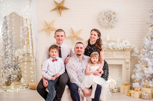 Familienporträt im Studio für das neue Jahr dekoriert. Weihnachtsfamilienabend. Familie zu versammeln umarmen und lächeln. dekoriertes Wohnzimmer mit Kamin und Weihnachtsbaum