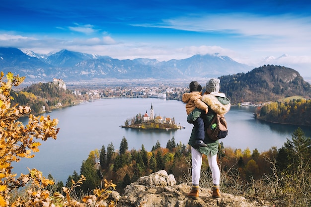 Familienreisen Europa. Mutter mit Sohn, der auf Bleder See schaut. Herbst oder Winter in Slowenien, Europa. Blick von oben auf die Insel mit der katholischen Kirche im Bleder See mit Schloss und Bergen im Hintergrund.