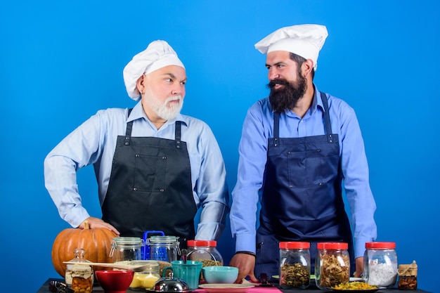 Familienrestaurant Ältere bärtige Männer Professionelle Restaurantköche Kochmänner kochen Essen zubereiten Kulinarisches Rezept Kulinarisches Buch Ausgewählte Zutaten Hausgemachte Mahlzeit Vater und Sohn kulinarisches Hobby