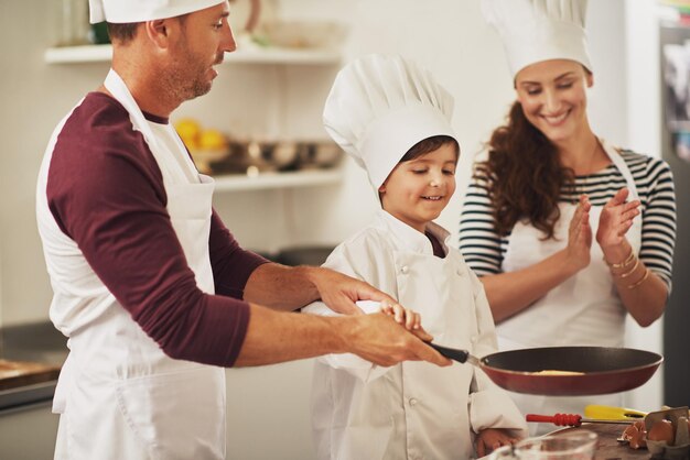 Familienspaß in der Küche Aufnahme einer lächelnden Familie, die gemeinsam Pfannkuchen in der Küche zubereitet