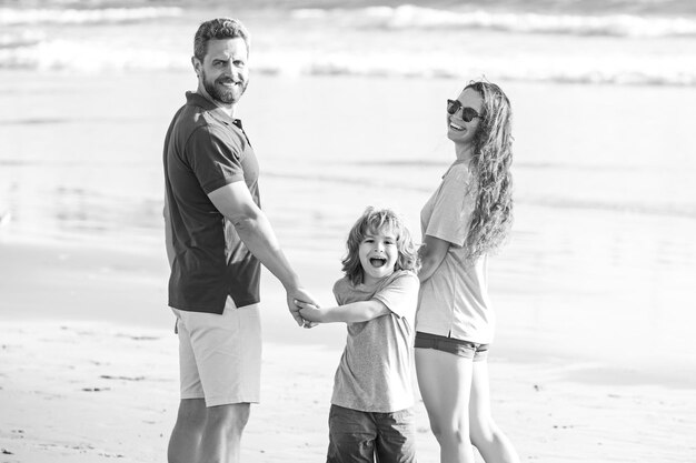 Familienspaziergang am Meeresstrand glückliche Eltern mit Kind, das am Strand spielt und die Sommerzeit in der Natur verbringt