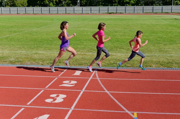 Familiensport und Eignung, glückliche Mutter und Kinder, die draußen auf Stadionsbahn laufen, Kindergesundes aktives Lebensstilkonzept