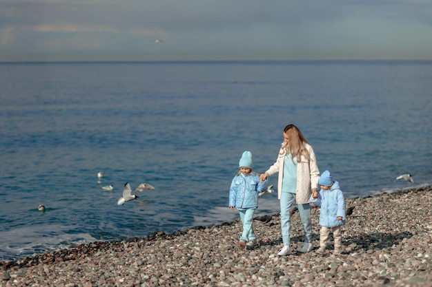 Familienurlaub am Meer in der Nebensaison glückliche Mutter und Kinder, die entlang der Küste spazieren