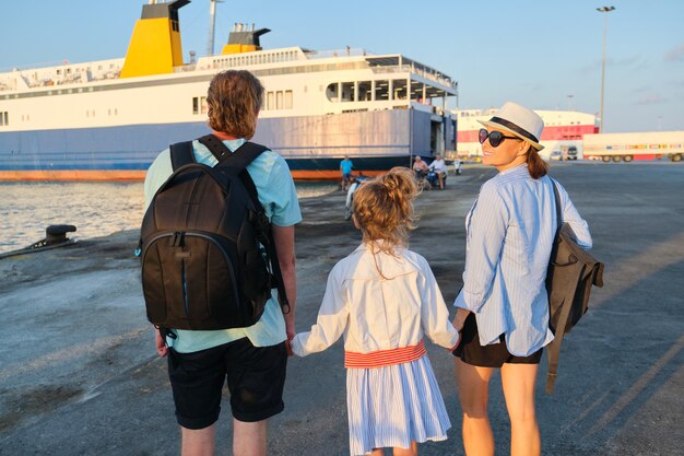 Familienurlaub am Meer, Mutter, Vater und Tochter, Kind im Hafen, Händchen haltend mit Blick auf die Fähre