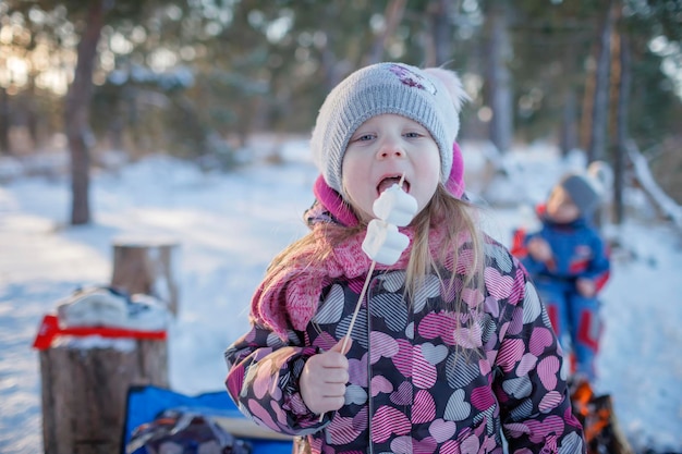 Familienwinterpicknick kleines Mädchen sitzt am Lagerfeuer im verschneiten Wald aktives Wochenende