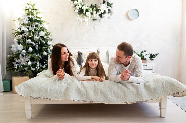 Familyat casa perto de árvore de Natal na cama