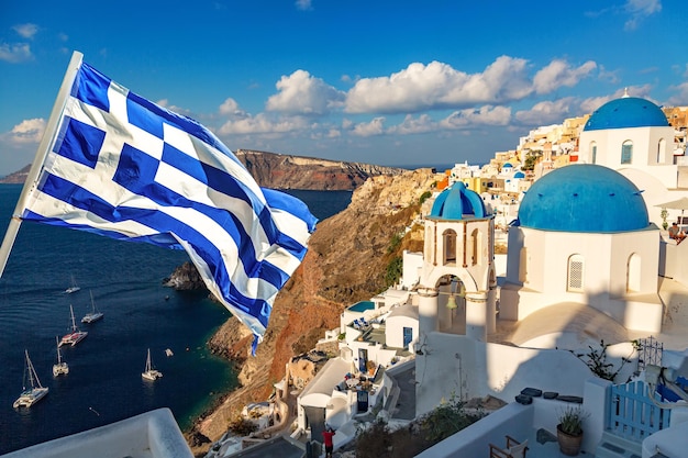 Famosa vista de Santorini Três cúpulas azuis e casas brancas tradicionais com bandeira grega Oia vila Santorini ilha Grécia