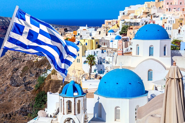 Famosa vista de Santorini Tres cúpulas azules y casas blancas tradicionales con bandera griega Pueblo de Oia Isla de Santorini Grecia