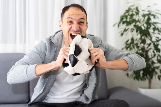 Foto fan del fubol. chico emocional gritando celebrando la victoria del equipo sosteniendo la bola posando en el fondo del estudio. foto de alta calidad