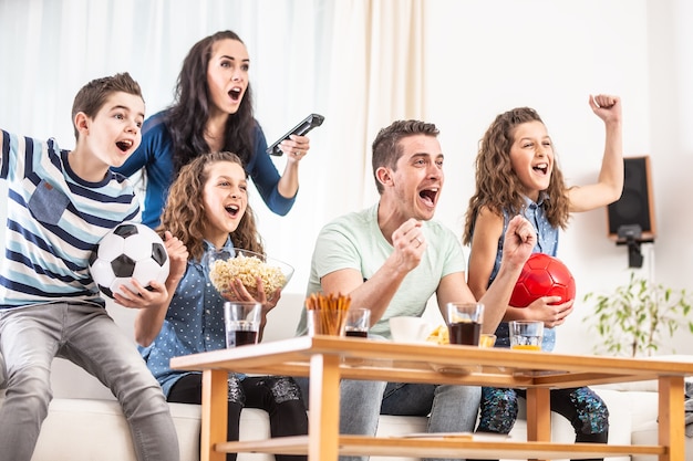 Fanáticos delirantes animando a los deportes, mientras una familia de cinco miembros ven fútbol, juegan en la televisión en casa, gritando de alegría.