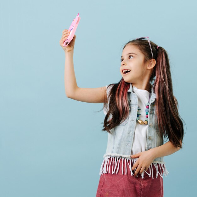 Fancy tween girl en falda de chaqueta de jeans tomando un selfie mirando hacia arriba