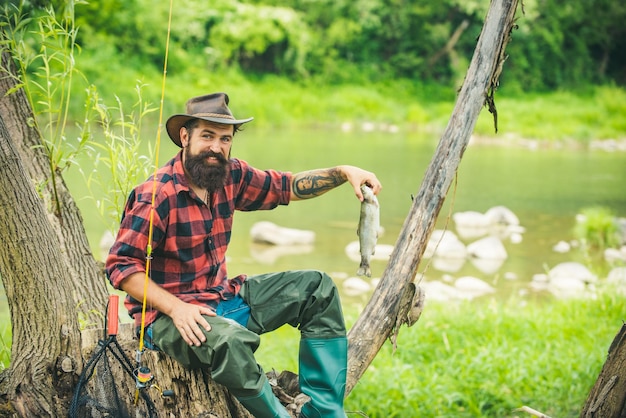 Fangen und Fischen Fisch, der normalerweise in freier Wildbahn gefangen wird Mann am Flussufer genießt friedliche idyllische Landschaft beim Fischen Eleganter bärtiger brutaler Hipster-Mann, der mit Fisch fischt