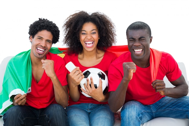 Fans del fútbol que animan en rojo que se sientan en el sofá con la bandera de Portugal