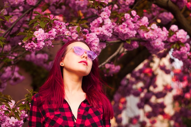 Fantasia Magical Spring Garden e mulher sonhadora. Garota de óculos cor de rosa com cabelo comprido rosa soprando. Primavera ou verão beleza adolescente sob as flores de sakura flor.