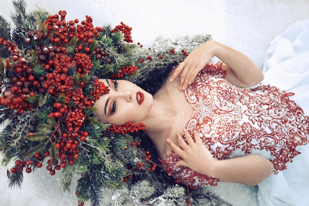 Foto fantasiekönigin in der krone aus roten beeren und fichtenzweigen liegt im schneewintermärchen