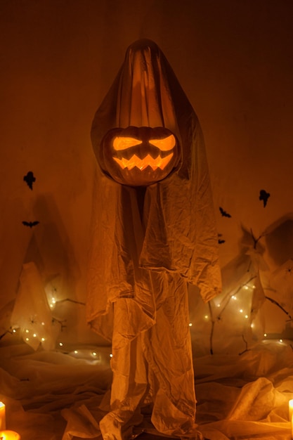 Fantasma assustador segurando Jack o lantern no fundo da teia de aranha com morcegos e luzes brilhantes no escuro Decorações de festa de halloween atmosférico assustador e pessoa sob lençóis Feliz Dia das Bruxas