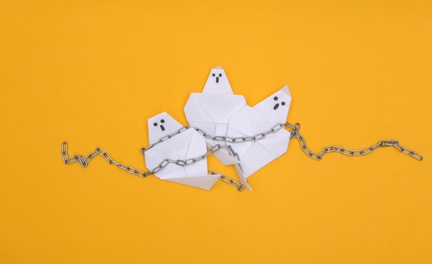 Foto fantasmas de origami con cadenas de acero sobre un fondo amarillo. tema de halloween