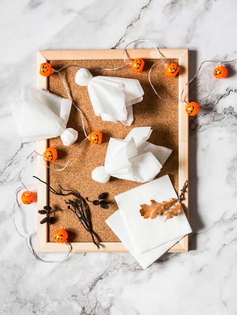 Fantasmas de papel caseros de Halloween en un tablero de corcho y una guirnalda de calabaza en una vista superior de fondo claro Creatividad del concepto