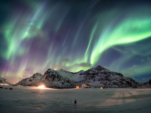 Fantástica aurora boreal sobre montaña nevada con hombre de pie